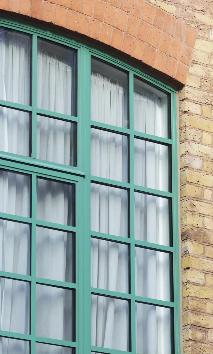 A green-framed arched steel-look window in a brick building
